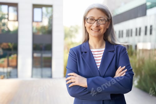 Preview: Portrait of a beautiful happy mature business woman in eyeglasses and classic wear keeping arms