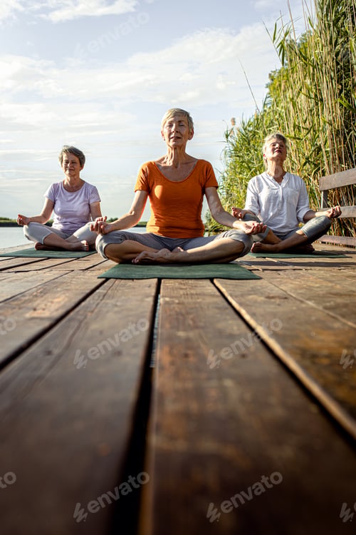 Preview: Group of senior woman doing yoga exercises by the lake.