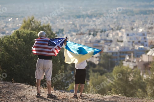 Preview: Retired man and kid boy holding the flags of the USA and Ukraine on city view