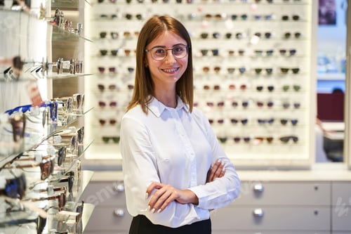 Preview: Cheerful young woman in glasses standing in optical store
