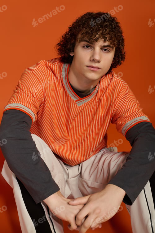 Preview: Curly-haired teenage boy in casual orange outfit against bright background