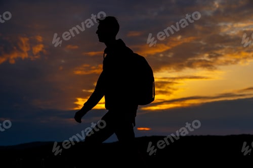 Preview: Silhouettes of hiker with backpack enjoying sunset view from top of a mountain