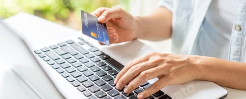 Preview: Young woman holding a credit card and using computer for making online payment shopping
