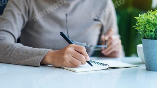 Preview: Closeup image of a woman writing on a blank notebook on the table