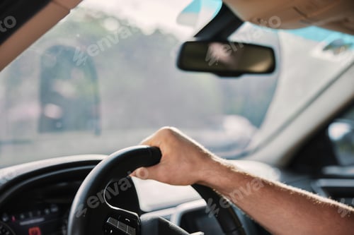 Preview: Hand gripping steering wheel inside a car with a blurred road view in the background