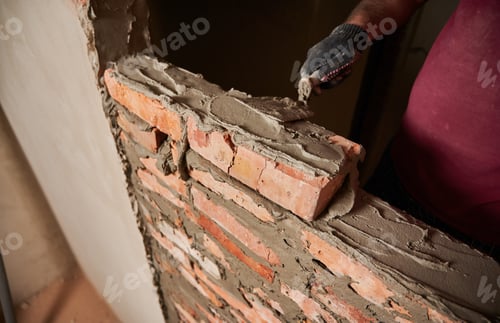 Preview: Male builder in work gloves building brick wall.