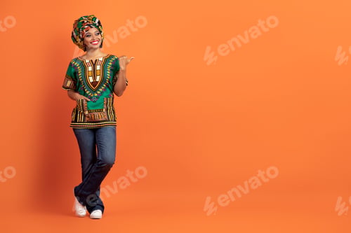 Preview: Cool black woman in african costume pointing at copy space