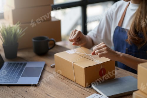 Preview: young woman, a happy Asian business owner preparing a parcel box and checking online purchases