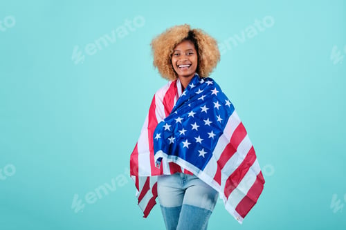 Preview: Smiling afro woman wrapped with an American flag while standing over an isolated background.
