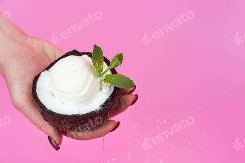 Preview: Vanilla ice cream balls in a fresh coconut half, decorated with mint leaves in your hand on a pink