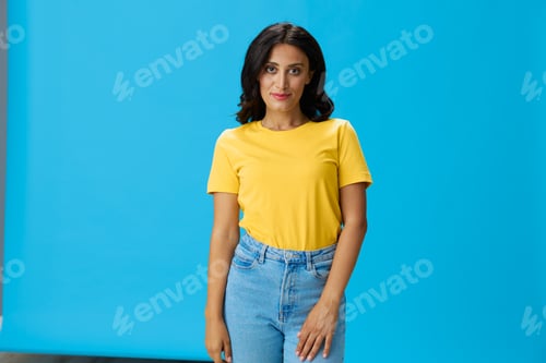Preview: Woman in yellow t-shirt on blue background posing gestures emotions and signals with smile, hands up