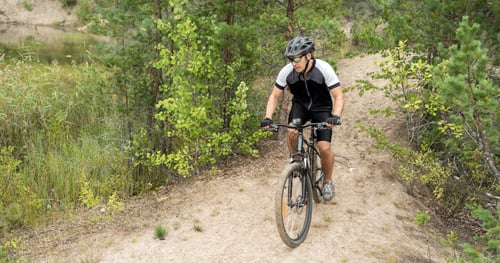 Preview: A man rides a mountain bike in a helmet and gear on the road in a green forest