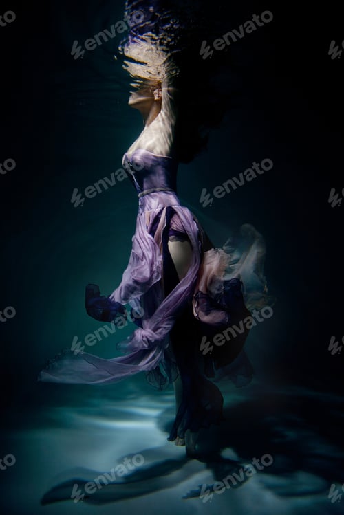 Preview: Woman in an extravagant purple designer dress underwater in the pool at underwater studio