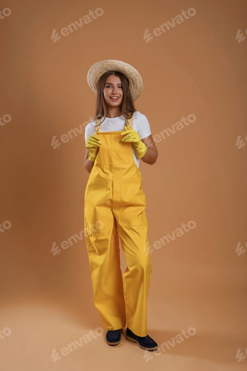 Preview: Garden worker is in straw hat. Young pretty woman is against background in the studio