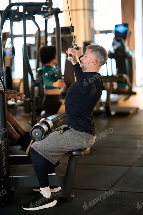 Preview: Mature man doing lat pulldown exercise in gym