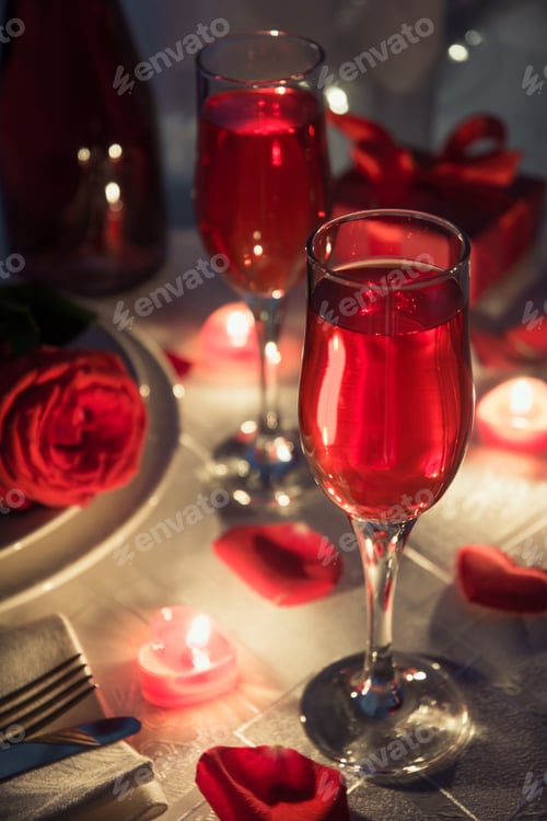 Preview: Setting of glasses with candles, champagne, bottle and gift box on romantic table.