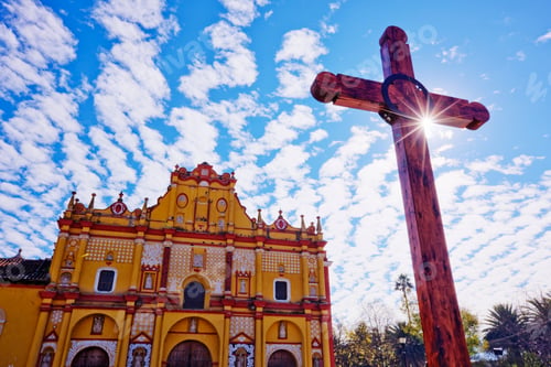 Preview: Crucifix in a courtyard in front of an ornate painted church.