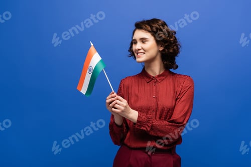 Preview: cheerful language teacher holding flag of India and looking at camera isolated on blue