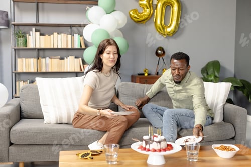 Preview: Celebrating birthday, friends enjoying cake and snacks on cozy living room sofa