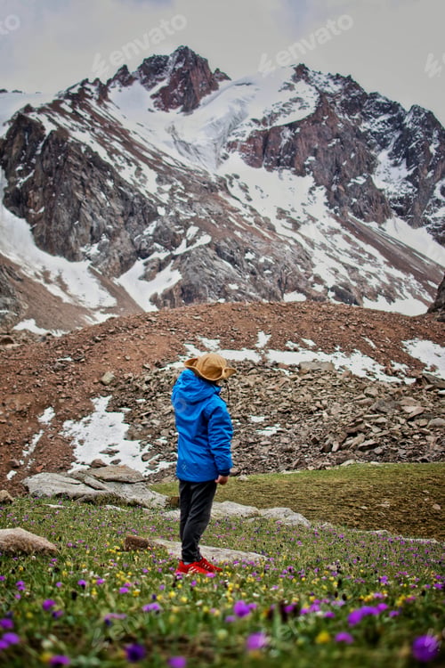 Preview: Rear view of a young boy in the cowboy hat on the hike standing at the foot of the snowy mountains