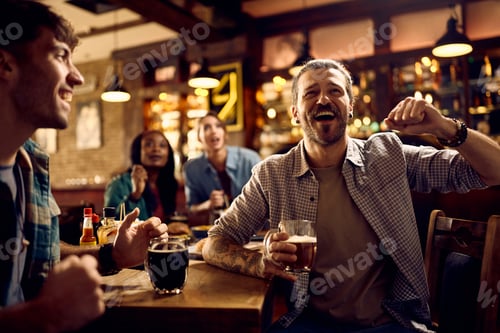 Preview: Young man and his friends cheering while watching sports game in a bar.