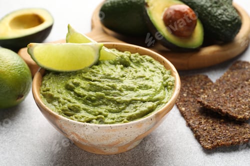 Preview: Tasty avocado dip, lime and crispbreads on light grey table, closeup