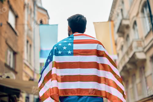 Preview: Rear view of patriotic sports fan covered with USA flag on the street.