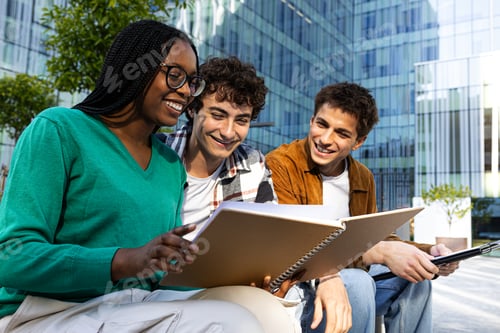 Preview: Multiracial college students studying together sitting on campus bench.