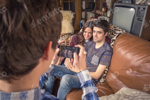Preview: Friend taking photos to teenage couple on a sofa