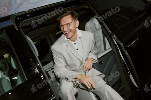 Preview: Smiling Male Celebrity in Grey Suit Sitting in Back Seat of Car