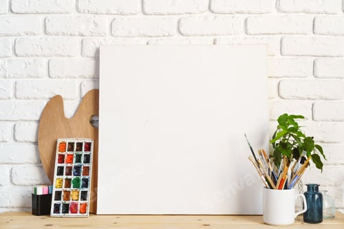 Preview: Photo frame as easel with artist's tools on wooden table against white brick wall