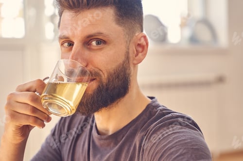 Preview: Handsome young man with beard drinking herbal tea
