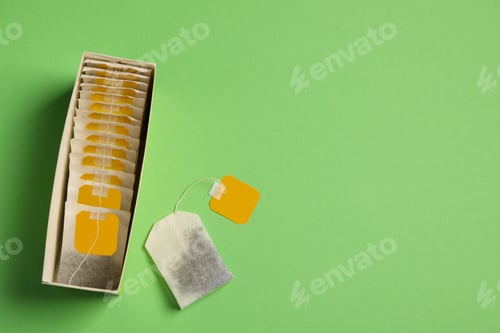 Preview: New tea bags with tabs and box on green background, flat lay. Space for text