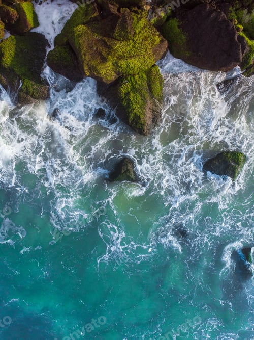 Preview: Vertical overhead aerial shot of a wavy blue sea against the rocks