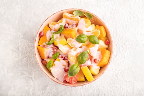 Preview: Vegetarian fruit salad of yogurt pumpkin, tangerine, basil microgreen on gray, top view, close up.