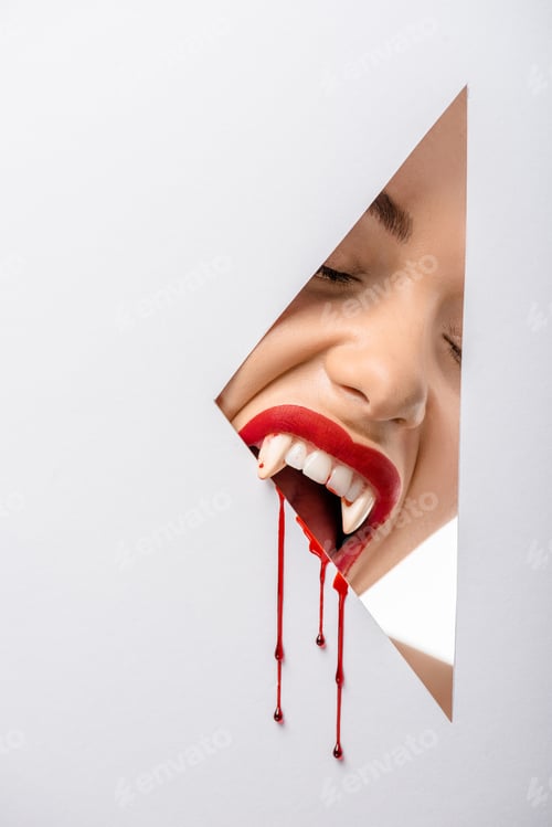 Preview: cropped shot of woman with vampire teeth and blood biting through hole on white
