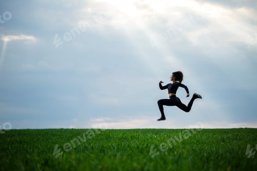 Preview: Young professional gymnast is jumping in nature against the blue sky. Girl athlete in a black top