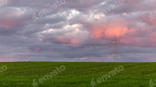 Preview: High voltage line in a green farmland against cloudy sky at sunset