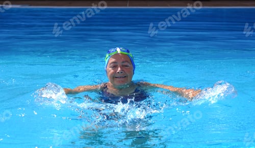 Preview: Senior sporty woman smiling while swimming in outdoor swimming pool on a sunny day