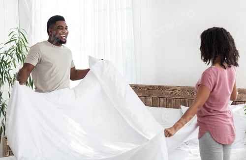 Preview: African cheerful couple making bed after sleeping in morning