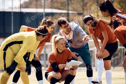 Preview: Young coach giving instructions to his female soccer team on playing field.