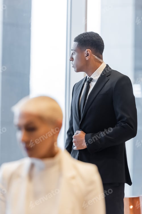 Preview: african american security man in earpiece near senior businesswoman on blurred foreground