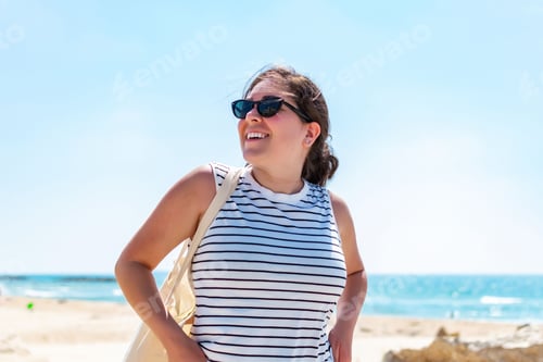 Preview: Happy woman in sunglasses at the beach, smiling and looking around on a sunny summer day