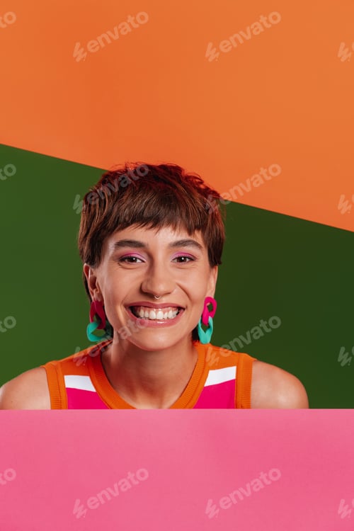 Preview: Happy young woman looking out of the colorful banners while standing against background