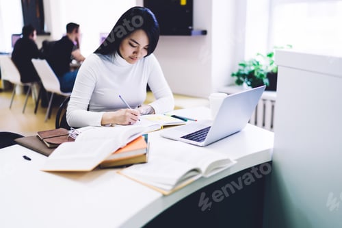 Preview: Focused Young Woman Studying at Desk with Laptop