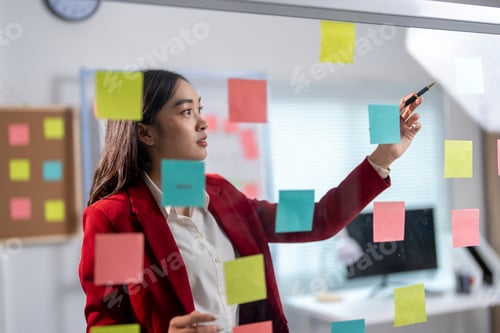Preview: Young manager planning project using adhesive notes on glass wall in office