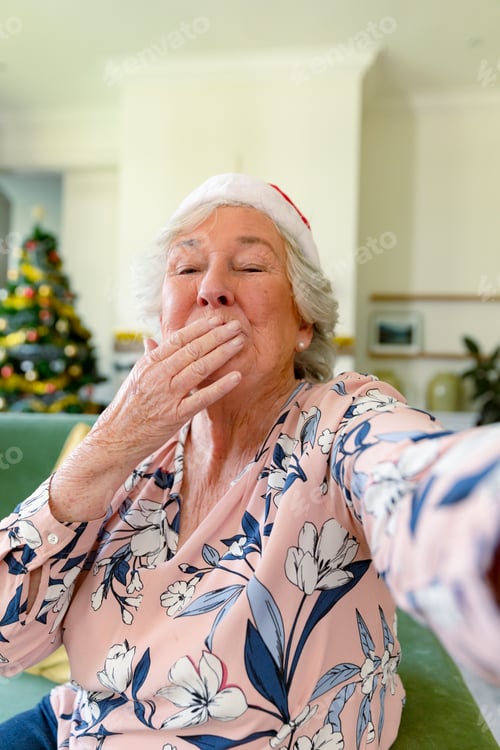 Preview: Happy caucasian senior woman wearing santa hat having video call, sending kisses at christmas time