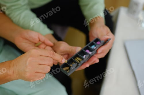 Preview: Closeup elderly woman putting pills into pill organizer. Health care concept.