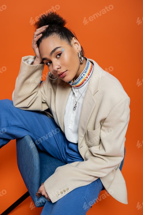 Preview: stylish african american fashion model in smart outfit with vivid makeup looking at camera