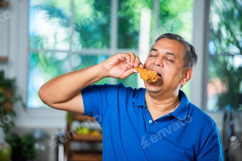 Preview: Indian asian mid age handsome man eating chicken leg piece with happiness